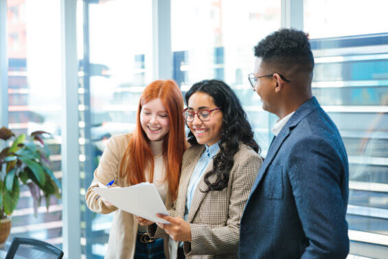 Young professionals starting their careers after college review documents together near large office windows.