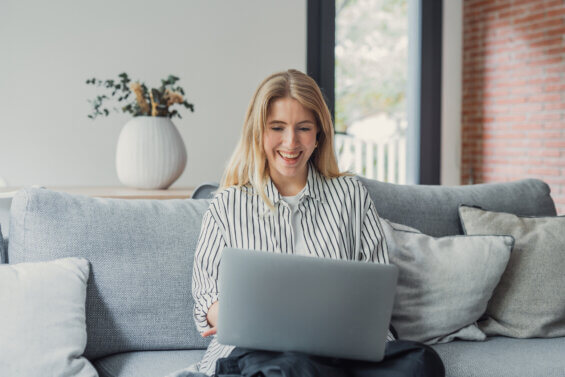 Recent college graduate smiles while searching for jobs on her laptop from home.