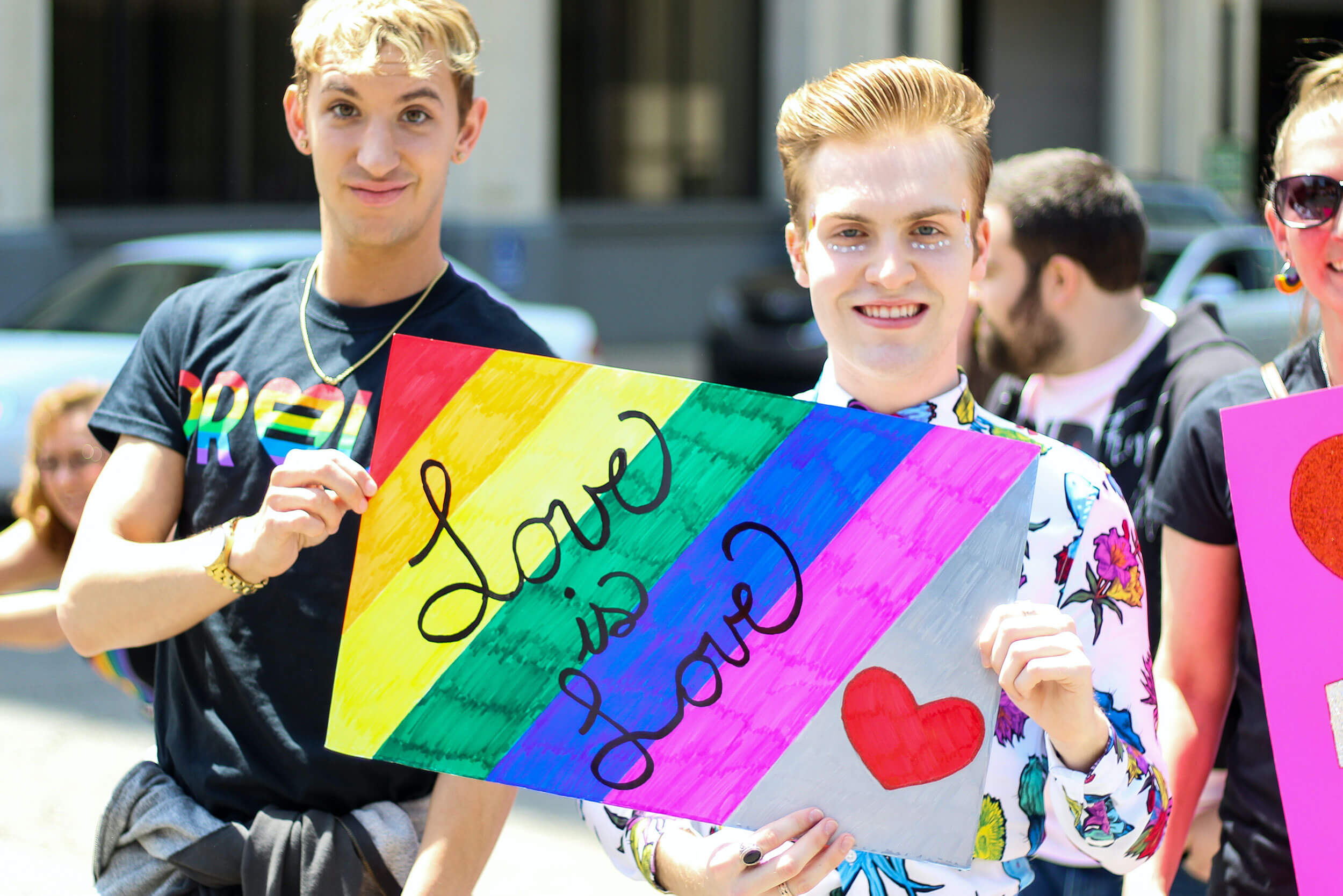 Two people hold a rainbow sign which states "Love is Love."