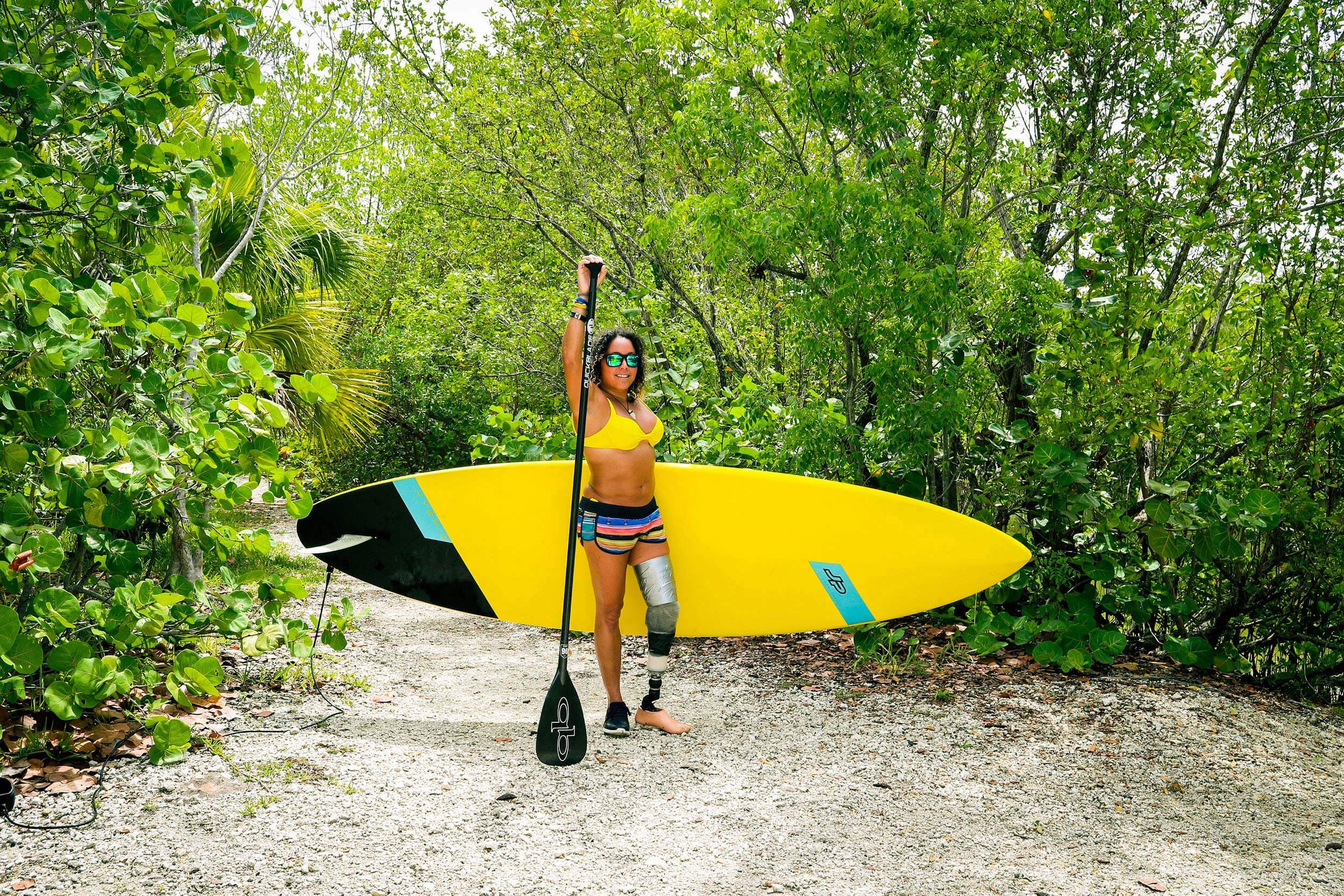 Woman stands on dirt trail holding paddleboard.