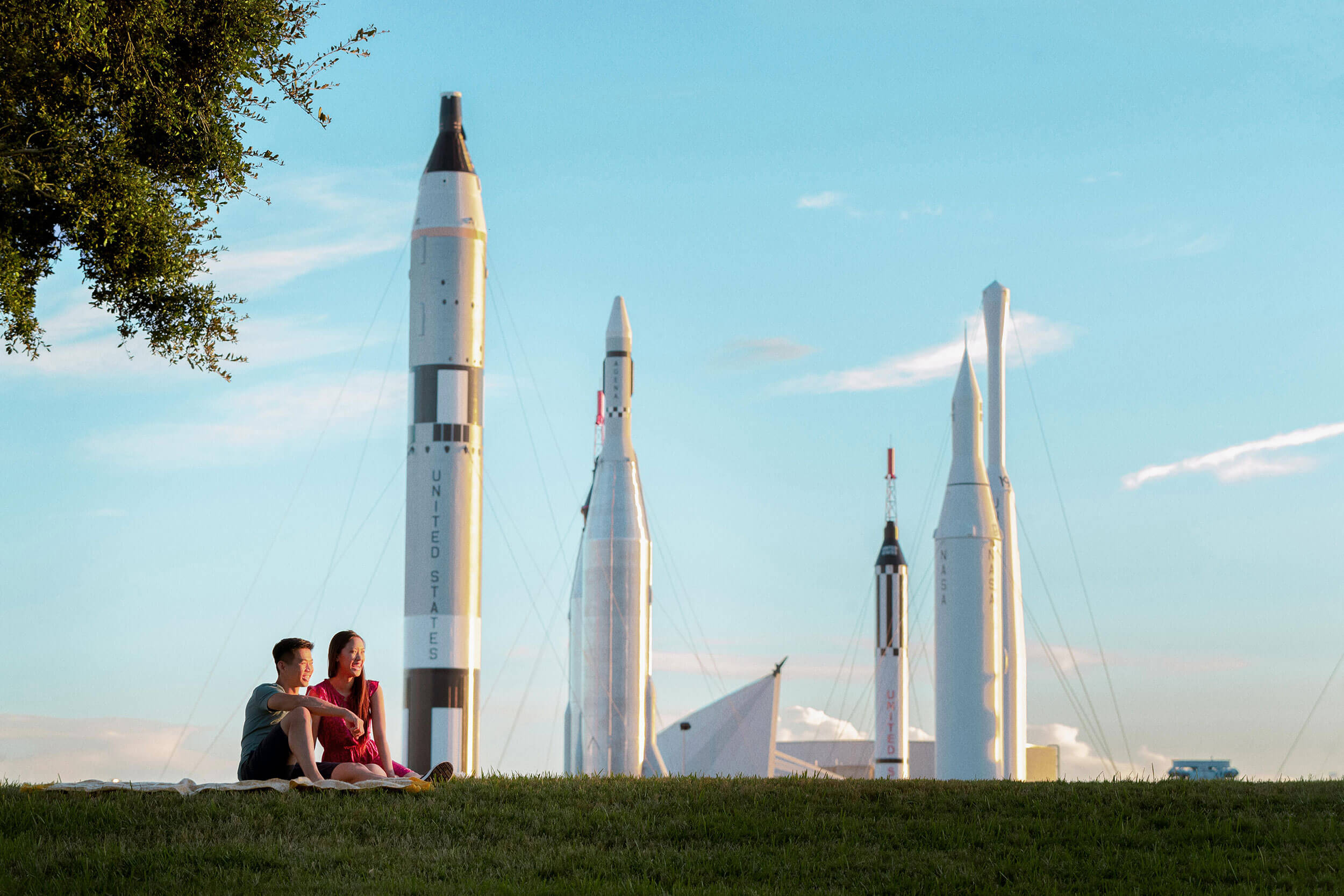 Couple sitting on grass in front of rockets.