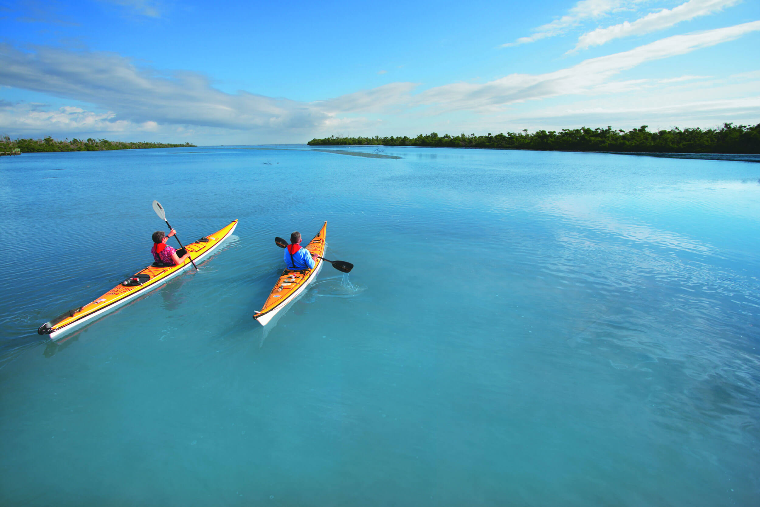 Two people kayak in bright blue bay.
